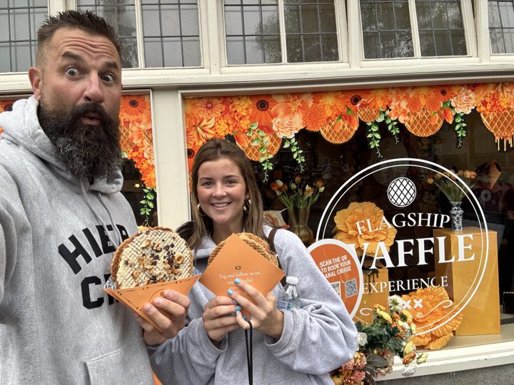 Two people enjoying waffles outside a shop